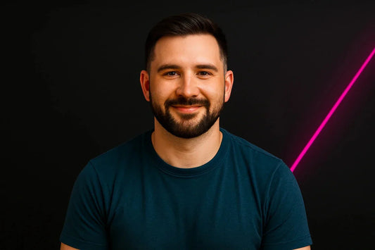 junger Mann mit Bart vor schwarzem Hintergrund mit pinkem Neon-Licht, lächelnd in die Kamera
