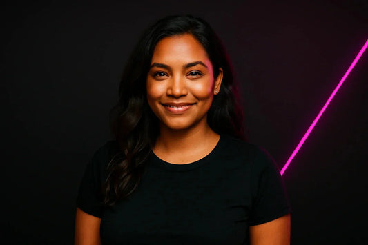 junge Frau mit dunklem Haar vor schwarzem Hintergrund mit pinkem Neon-Licht, lächelnd in die Kamera